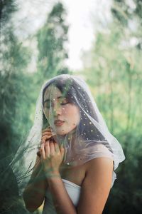 Woman with eyes closed wearing netting against trees