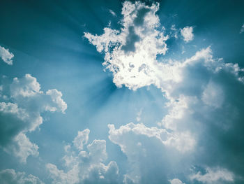 Low angle view of sunlight streaming through clouds