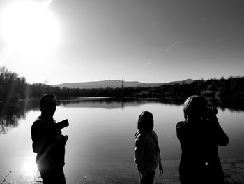 Rear view of people standing by lake against sky