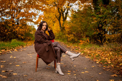 Portrait of a young woman with old armchair in a brown coat in autumn
