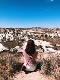 Rear view of woman sitting on landscape against clear blue sky