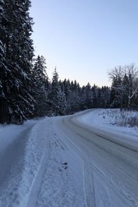 Road amidst snow covered trees against clear sky during winter