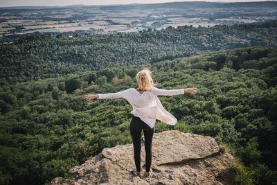 Rear view of woman standing with arms outstretched against forest