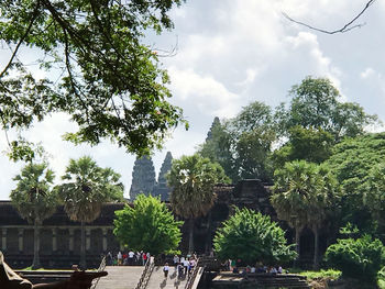 People by trees in city against sky