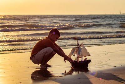 Boy on beach against sky during sunset