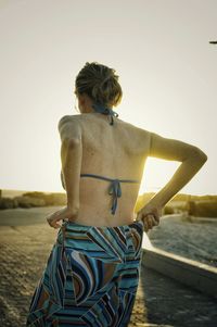 Rear view of woman getting dresses at beach during sunset