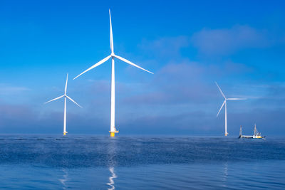 Wind turbines in sea against blue sky