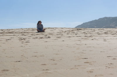 Woman sitting on sand at beach against clear sky