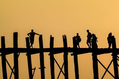 Silhouette people on pier against clear orange sky