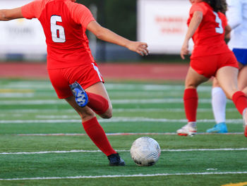 Female soccer player kicking the ball downfield to her teammate during a game.