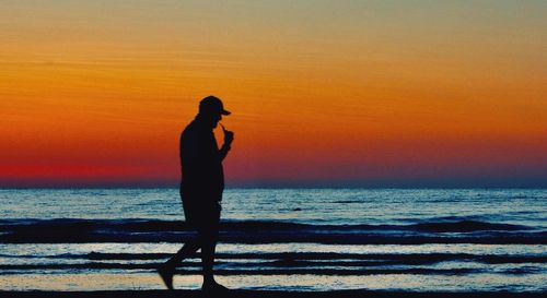 Silhouette man standing on beach against orange sky