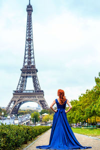 Rear view of bride in blue dress standing on footpath against eiffel tower