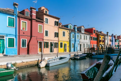 Boats moored in canal by buildings against sky