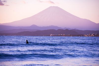 Silhouette man swimming in sea against mt fuji during sunset