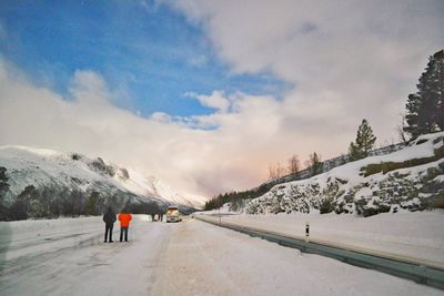 People walking on snowcapped mountain road against sky