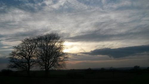 Silhouette of trees on landscape against cloudy sky