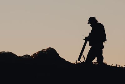 Silhouette man standing on mountain against clear sky during sunset