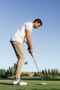 Professional male golf player preparing to hit ball with putter in green field while looking down on summer day