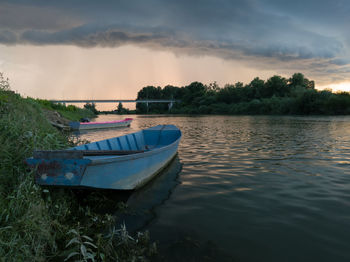 Boat moored in river against sky during sunset