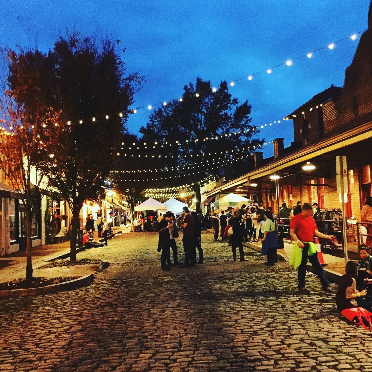 architecture, building exterior, built structure, sky, large group of people, illuminated, city, tree, street, person, men, street light, lifestyles, city life, night, walking, leisure activity, dusk, outdoors