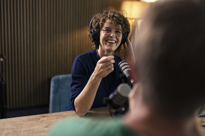 Happy presenter wearing eyeglasses talking with guest in radio station