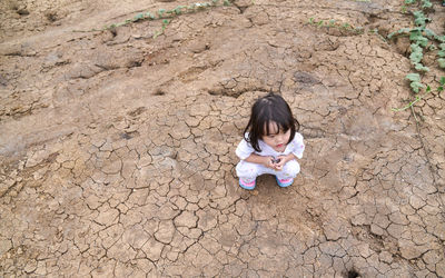 High angle view of girl crouching on drought land