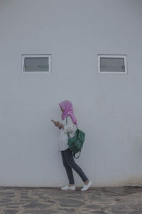 Side view of young woman with backpack walking by wall