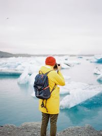 Rear view of tourist photographing glacier in lake during winter
