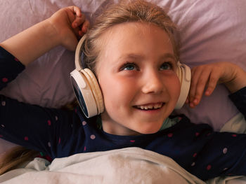 Child girl in headphones learns language listen to music podcast in smartphone online in bed at home