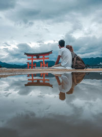 Rear view of men with reflection in water against sky