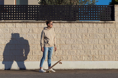 Young man looking to the side sun stepping on skate board against white wall in the afternoon light