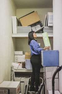 Saleswoman with appliance standing on ladder at electronics store