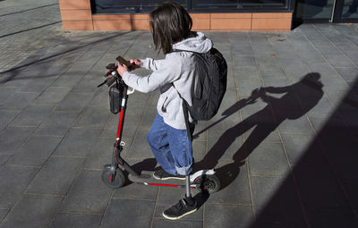 Young disabled man using smart phone while standing on electric push scooter during sunny day