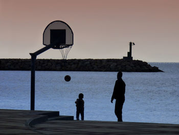 Men standing on basketball hoop against sky during sunset