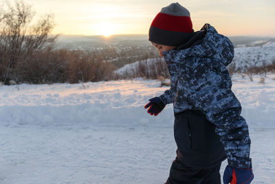 Young boy walking on a snowy park at sunset