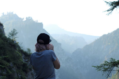 Rear view of woman wearing cap while standing against mountains