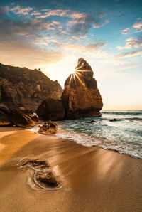 Rocks on beach against sky during sunset