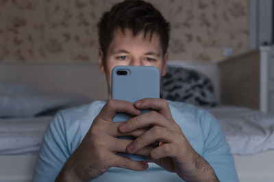 Addicted men sitting near bed and surfing in web with smartphone. social media and phone dependency