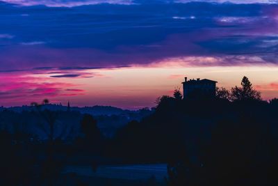 Silhouette trees and buildings against sky at sunset