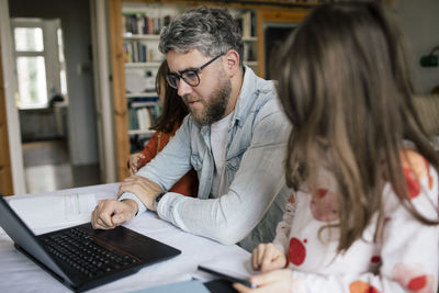 Mid adult man using laptop by daughters at home