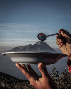 Optical illusion of hands holding mountain in plate against sky