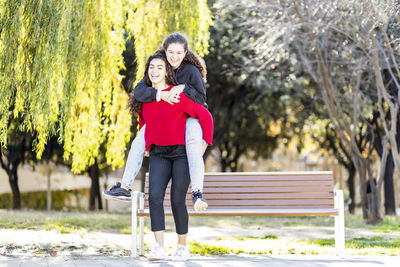 Happy teenage girl giving piggyback ride to friend in park
