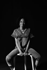 Portrait of young woman sitting on chair against black background