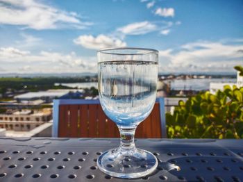 Glass of water on table by sea against sky