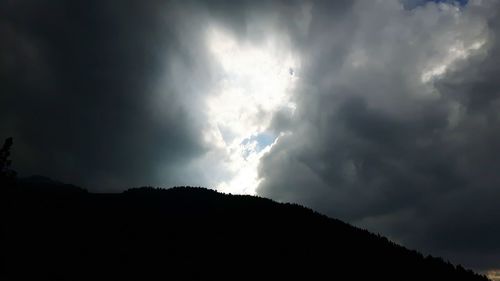 Low angle view of storm clouds over silhouette mountain