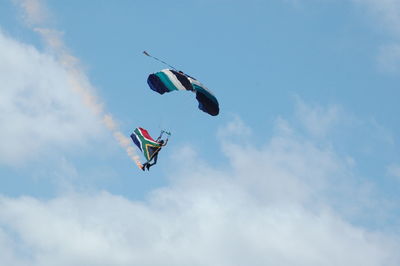 Low angle view of man with south african flag paragliding against cloudy sky