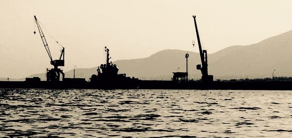 Silhouette cranes by sea against sky during sunset