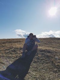 Man photographing while sitting on land against sky