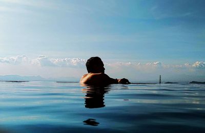 Rear view of man swimming in pool against sky