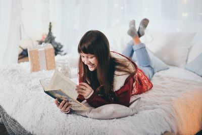 Young woman using mobile phone while sitting on bed at home